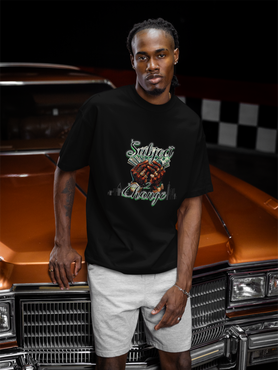 Man wearing a SUBJECT 2 CHANGE BRN and BLACK t-shirt with a graphic design standing in front of an orange car.