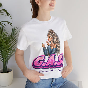 Person wearing a white t-shirt with a graphic design and text, standing indoors next to a plant. G.A.S. 3